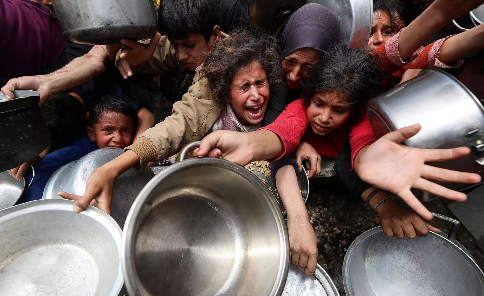 Children holding empty pots at a community kitchen in Gaza
