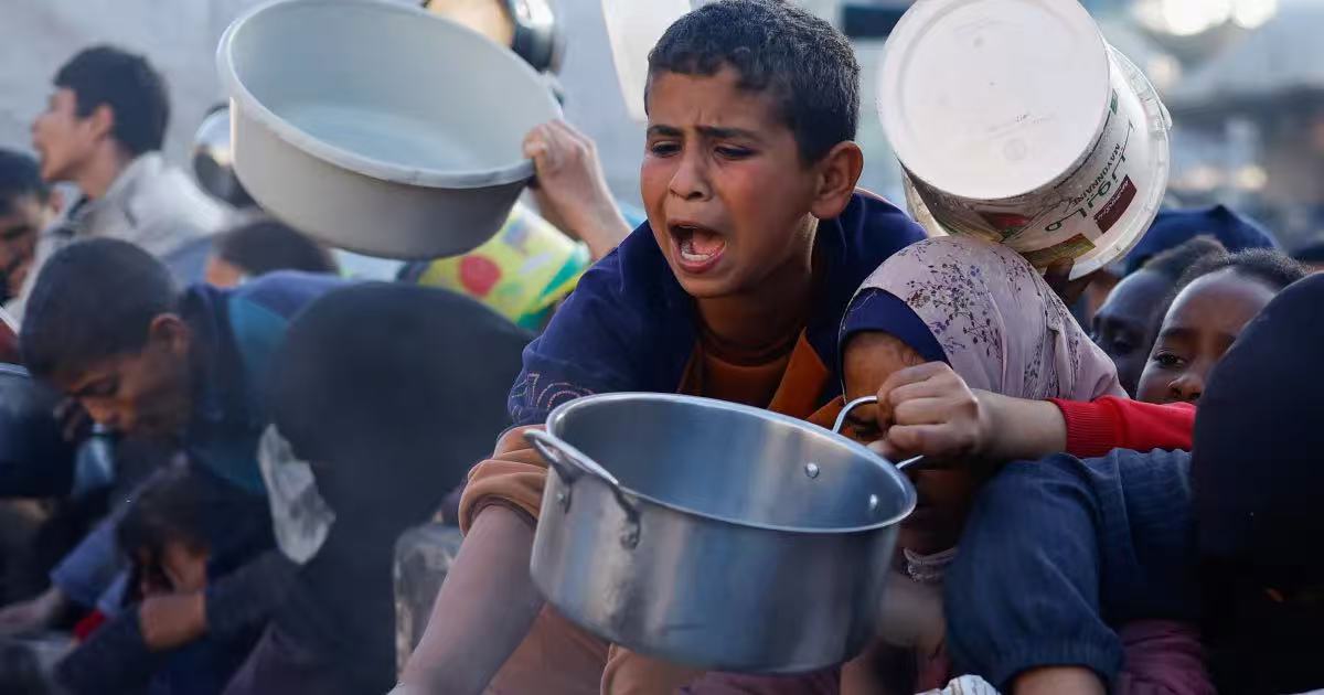 A boy waits with his pot at a food distribution point
